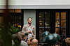 Man with lanyard speaking to an audience in an indoor seminar space.