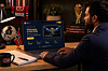 A man sits at a desk using a laptop displaying a football prediction website, with Norway flags, a notebook, and a trophy in the background.